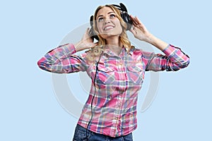 Portrait of smiling young woman listening to music in headphones and looking up.