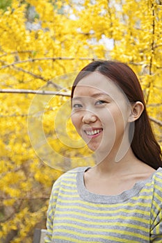 Portrait of smiling young woman with long hair outdoors in the park in springtime with yellow blossoms