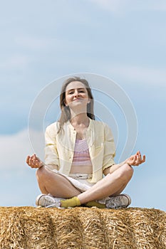 Portrait of smiling young woman meditating sitting in the hay against blue sky. Unity with nature