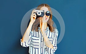 Portrait smiling young woman photographer with vintage film camera over blue wall