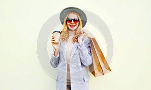 Portrait smiling young woman with shopping bags, holding coffee cup, wearing pink coat, round hat