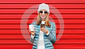 Portrait of smiling young woman with smartphone wearing jacket, white hat on red background