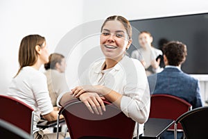 Portrait of smiling young woman smiling at camera during studying of foreign language with group of students in class