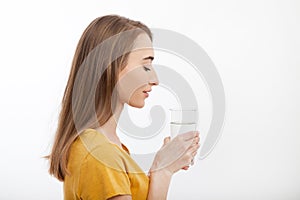 Portrait of smiling young woman standing in profile and holding a glass of water. white background. mock up.