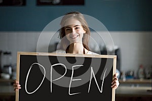 Smiling woman holding open sign chalkboard inviting to new cafe