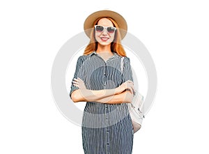 Portrait of smiling young woman wearing summer straw hat, striped dress and backpack isolated on white background