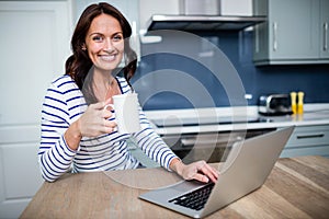 Portrait of smiling young woman working on laptop while holding coffee mug