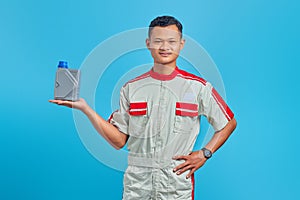 Portrait of smilling young asian mechanic showing engine oil plastic bottle in palm over blue background