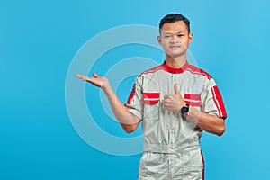 Portrait of smilling young Asian mechanic showing palm hands and thumbs up over blue background