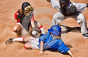 Portrait of Softball player sliding into home plate while umpire rules safe