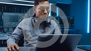 Portrait of Software Developer / Hacker / Programmer Sitting at His Desk and Working on Laptop Com
