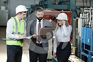 Portrait of a solid businessman with his secretary and factory engineer holding laptop, talking about factory financial report