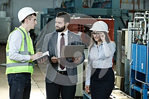 Portrait of a solid businessman with his secretary and factory engineer holding laptop, talking about factory financial report