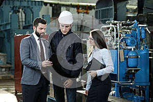 Portrait of a solid businessman with his secretary and factory engineer holding tablet, talking about factory financial report