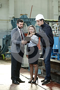 Portrait of a solid businessman with his secretary and factory engineer holding tablet, talking about factory financial report