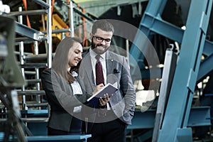 Portrait of a solid businessman with his secretary holding blue notebook, talking about factory financial report