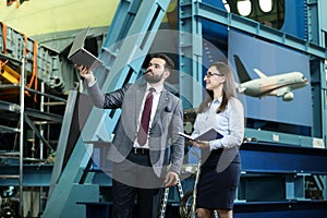 Portrait of a solid businessman with his secretary holding laptop and notebook, talking about factory financial report