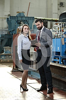 Portrait of a solid businessman with his secretary holding laptop and tablet, talking about factory financial report