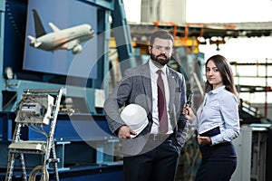 Portrait of a solid businessman with his secretary holding white hard hat, talking about factory financial report