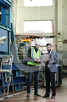 Portrait of a solid businessman with laptop and factory engineer controlling work process in a airplane factory.