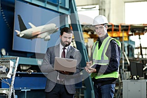 Portrait of a solid businessman with laptop and factory engineer controlling work process in a airplane factory.