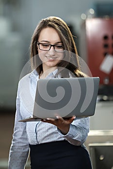 Portrait of a solid businesswoman holding laptop , controlling work process in a airplane manufactory.