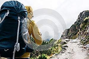 Portrait of solo hiker wearing professional backpack walk across foggy mountains way. Man tourist traveling along by rocky track