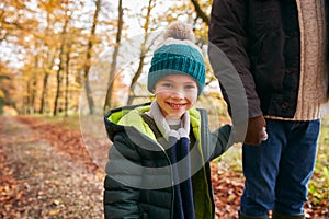 Portrait Of Son Holding Fathers Hand On Family Walk Through Autumn Woodland Landscape