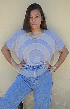 Portrait of a south asian young girl standing against yellow wall posing with her hands on hips with looking at camera