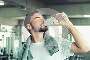 Portrait of Sport Man in Fitness Club and Drinking a Bottle of Water After Braking Exercised on Bodybuilding Equipment Background