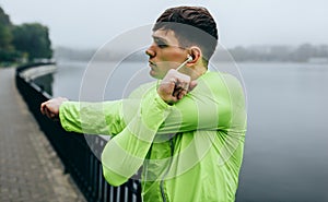 Portrait of sportsman stretching outdoor in the city lake background. Fitness male exercising in the park, wearing green and black