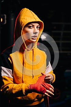 Portrait of sportswoman boxer in yellow sweatshirt pulls red bandages on her hands,