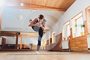 Portrait of sporty beautiful blond young woman in sportswear working out indoors, doing balance back bend, Natarajasana