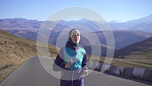 Portrait of a sporty muslim woman in hijab running on a sunny road on the background mountains