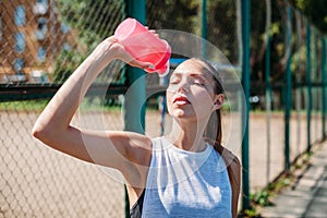 Portrait of sporty young woman drinking cool water from bottle on a summer sports field outdoors