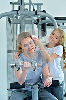 Portrait of sporty young woman and her daughter training with dumbbell in gym
