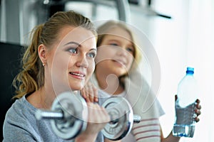 Portrait of sporty young woman and her daughter training with dumbbell in gym