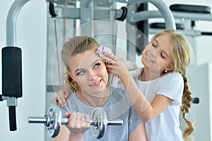 Portrait of sporty young woman and her daughter training with dumbbell in gym