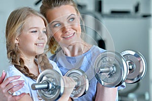 Portrait of sporty young woman and her daughter training with dumbbells in gym