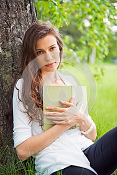 Portrait of spring brunette girl seating outdoor at the tree wit