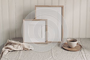 Portrait and square empty wooden frame mockups with cup of coffee. Beige linen table cloth. White beadboard wainscot