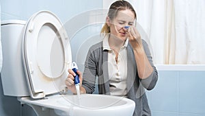 Portrait of squeamish young woman putting clothespin on her nose before washing toilet