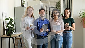 Portrait of standing smiling team with documents looking at camera.