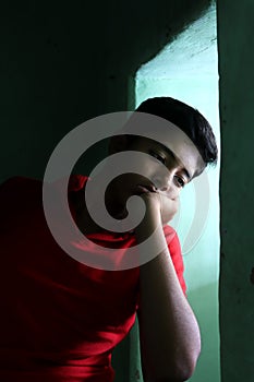 Portrait of a stressed Asian boy in front of window. An Indian melancholy boy is thinking. Sadness expression of a boy