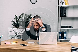 portrait of stressed businessman sitting at workplace with laptop