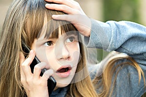 Portrait of stressed child girl with long hair talking on cell phone. Little female kid communicating using smartphone. Children