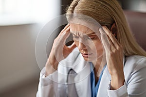 Portrait Of Stressed Female Doctor In Medical Coat Suffering Headache At Workplace