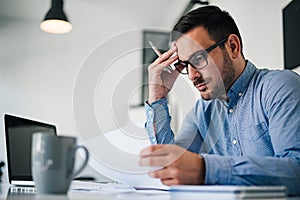 Portrait of stressed out and worried troublesome overworked businessman entrepreneur looking documents report in modern bright photo