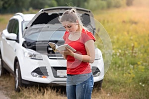Portrait of stressed woman standing at broken car and reading ow photo