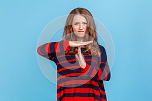 Portrait of stressed woman wearing striped casual style sweater showing time out gesture, looking